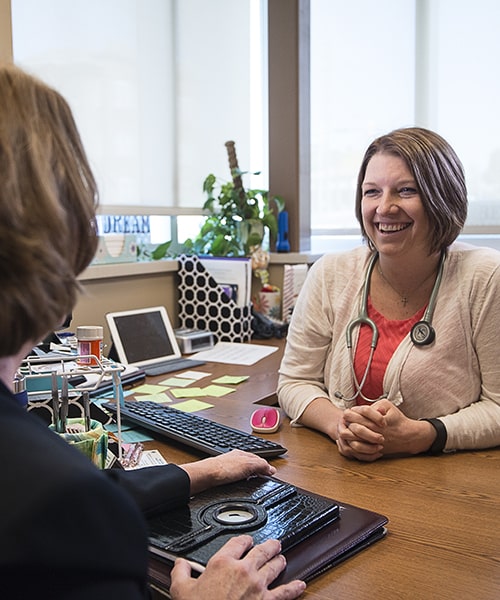 Female Doctor of Nursing Practice sitting at her desk speaking with a co-worker. 