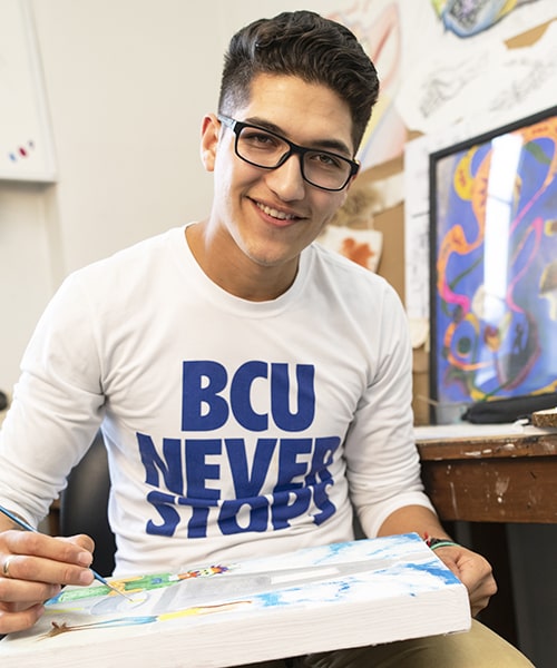 Hispanic male painting on a canvas in the North Hall art studio. 