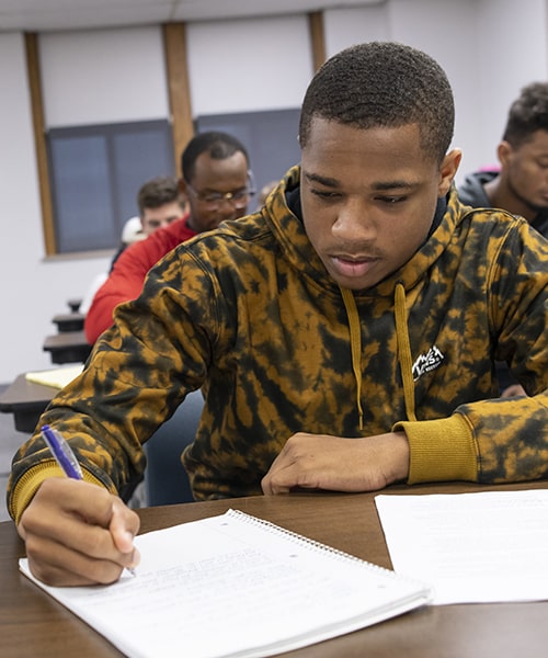 Male student taking notes during business class. 