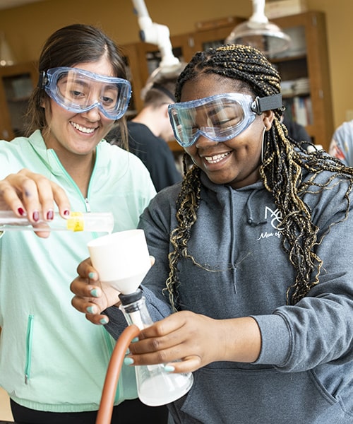 Female students pour chemicals while performing experiment in the chemistry lab. 