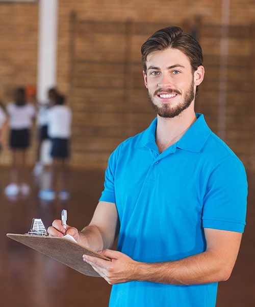 Physical Education instructor in gym with clipboard. 
