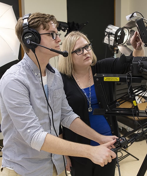 Male student learning how to operate camera equipment with guidance of professor.