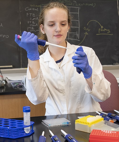 Female student measuring chemicals as she performs experiment.  